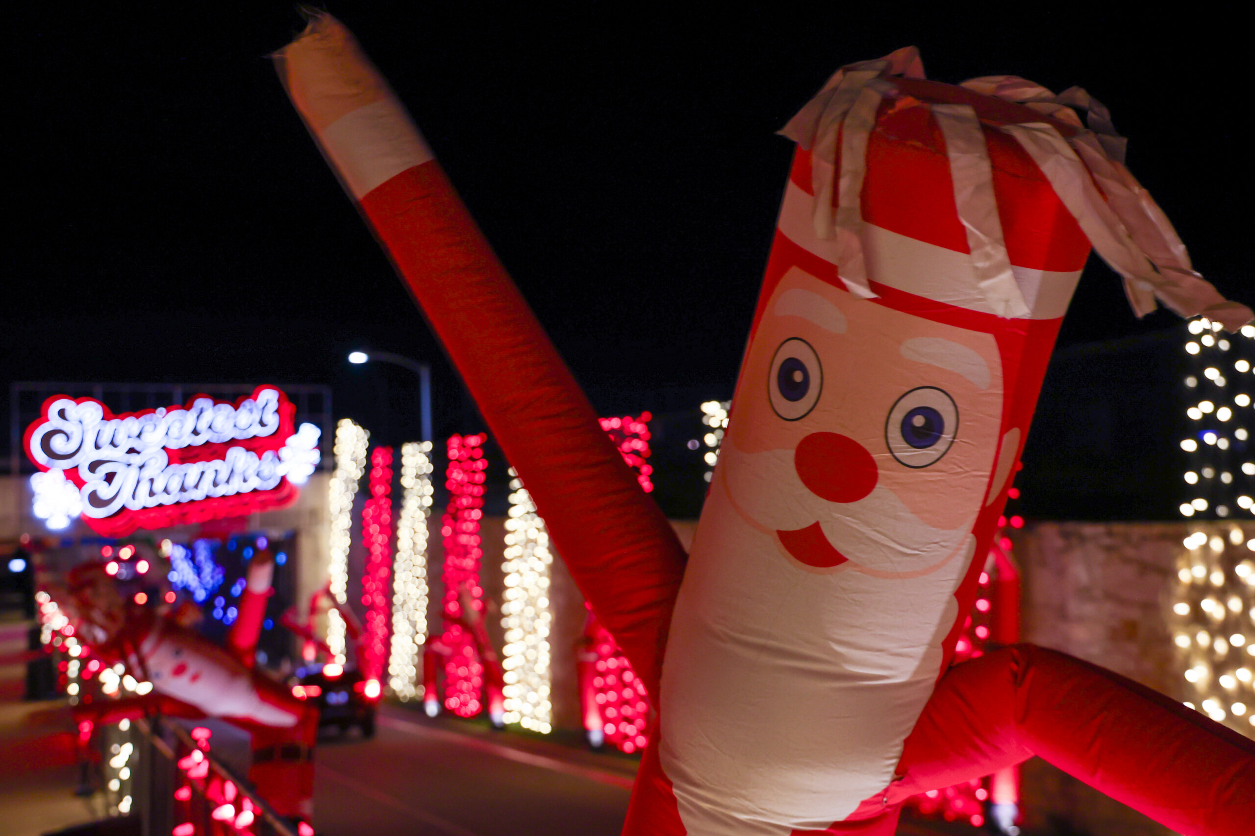 An inflatable Santa Claus figure stands in the foreground with Christmas lights and a "Sugafest Thanks" sign visible in the background at night.